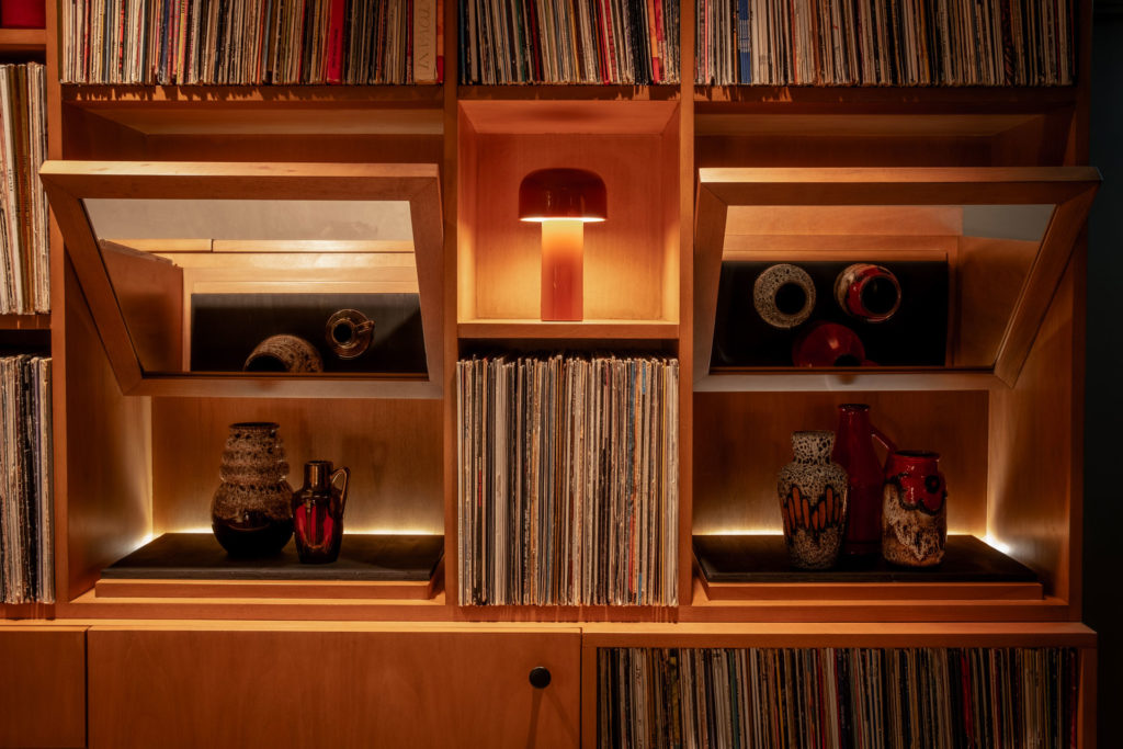 View of the interiors of the bar at Seed Library, which has stacks of Vinyl records and lowly lit lamps amongst wood shelving